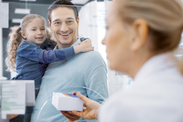 Take your pills. Blond female pharmacist transferring medication and man holding girl