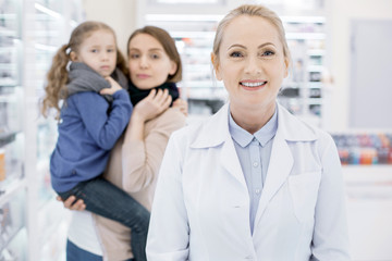 Fight against cold. Cheerful female pharmacist smiling to camera and posing on blurred background