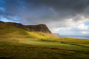 Beautifully captured moment on the west coast of the Isle of Sky in Scotland - setting sun shedding light over green fields, dark hills and vast meadows under the approaching storm
