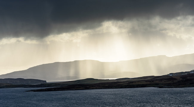 Rays of golden light through storm clouds hanging over the west coast of the Isle of Skye in Scotland - dark and moody image with high contrast, amazing views and impressive vistas