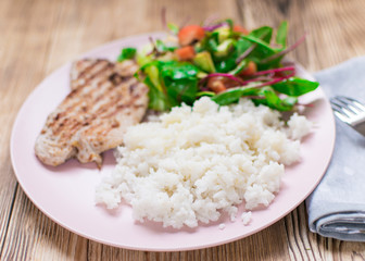 Grilled meat, boiled rice and vegetable salad on a wooden background.