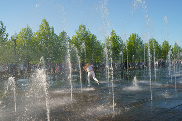 Girl running through the water jet of the fountains
