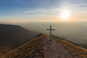 Cross on top of Mt. Serrasanta (Umbria, Italy), with warm golden hour colors and sun low on the horizon