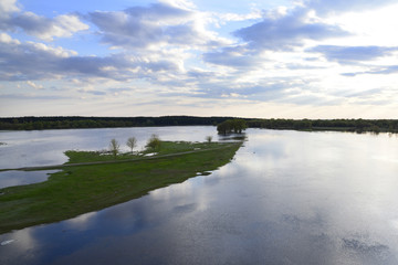 Photo of the spilling on the river in spring, green meadow and bright sky with small clouds