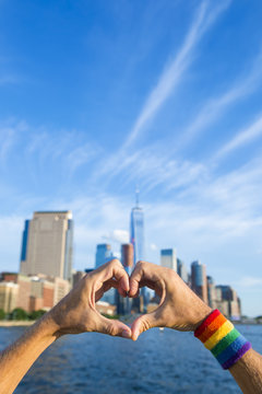 Hand wearing gay pride rainbow sweat band making 'number one' hand sign in front of city skyline
