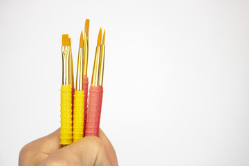 A hand holds bright pink and yellow paintbrushes on an isolated white background 
