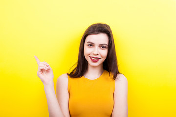 Smiling woman pointing up on yellow background