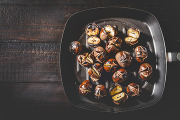 Roasted chestnuts in iron grilling pan over rustic wooden table.