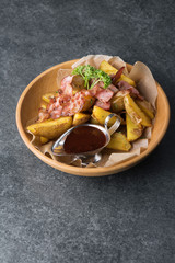 Fried potatoes with appetizing bacon and sauce are in a wooden plate