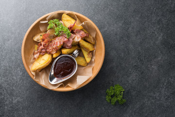 Fried potatoes with appetizing bacon and sauce are in a wooden plate
