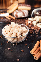 Brown sugar in a glass bowl next to candies and sweets on dark vintage wooden background