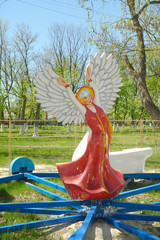 The statue of a girl in a long Russian folk sarafan dress hands like wings open and on the head kokoshnik in the form of a big star stands in the center of the children's carousel.