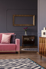 Empty gold frame hanging on wall with molding above retro cupboard with fresh purple tulips in...