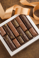 Handmade chocolate candies with golden splashes in box on wooden background