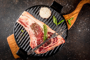 Raw beef marbled meat striplon rib eye steak with spices, grill pan, and herbs, dark background top view, copy space