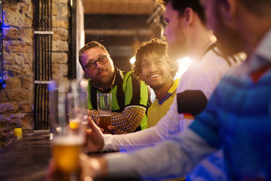 Soccer fans are sitting at the counter in the pub and are having a deep and friendly conversation about whose team is better, while drinking draft beer.