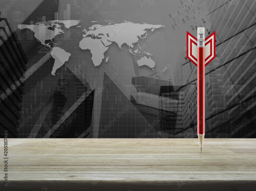 Poster red pencil in the shape of a dart on wooden table over world map with financial graph and modern cit