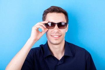 Cool man in casual shirt wearing sunglasses in studio photo on blue backgorund