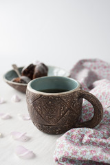 Clay cup with blue in the middle and a plate with a cupcake in the background. Items are on a white wooden background.