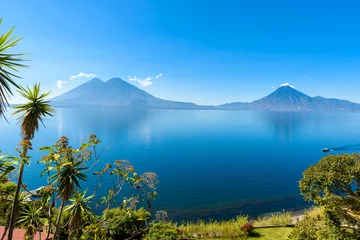 Schilderijen op glas View from Lake Atitlan in the early morning, blue skys and clear water, beautiful magic lake with volcanos and indigenous people in the highland of Guatemala  © Simon Dannhauer