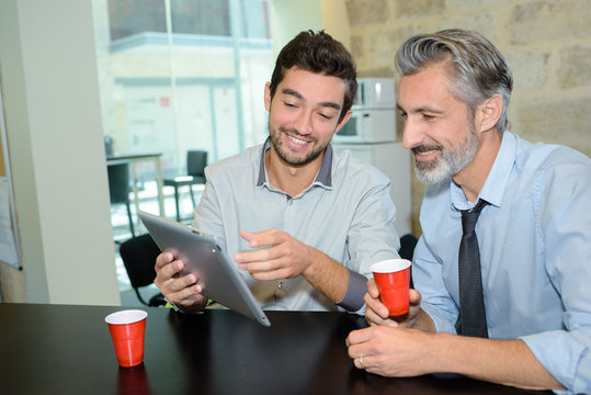 Men drinking coffee and looking at tablet
