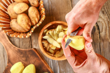 Men's hands clean potatoes for okroshki on an old wooden table.