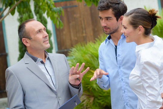 Realtor Talking To Young Couple In Front Of Property