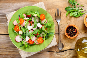 Vegetarian salad of arugula, tomato, radish and mozzarella cheese on an old wooden table.