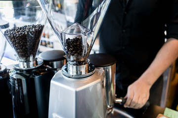 Young dedicated barista preparing coffee from fresh grinded roasted beans for a female customer in...