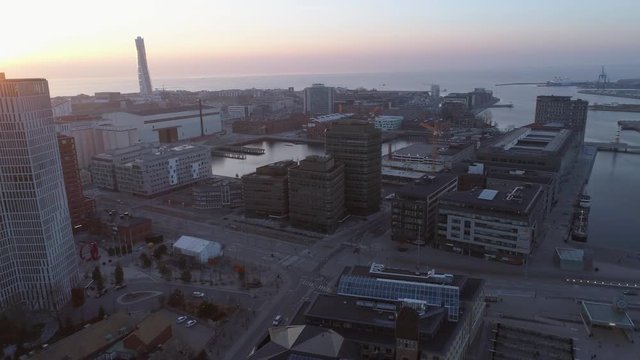 Aerial view of Malmö cityscape at sunset. Drone shot flying over city street, buildings and construction site at dusk. Business office buildings, tower cranes and sea coast, Sweden