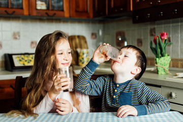 Children drink milk in the kitchen at the morning. Sister and brother prepare cocoa and have fun