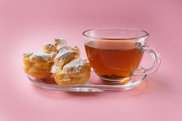 a cup of green tea and three profiteroles sprinkled with sugar powder on a pink background. homemade eclairs