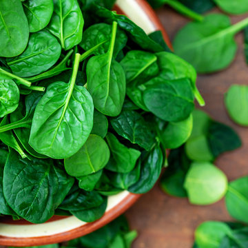 Fresh baby spinach leaves in a bowl on rustic wooden background, top view..