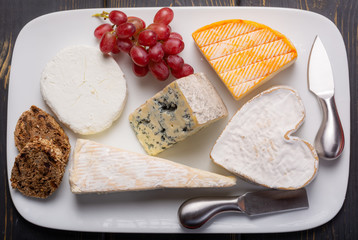 Flat lay, French cheeses plate in assortment, blue cheese, brie, munster, soft goat cheese, Neufchatel heart shaped cheese