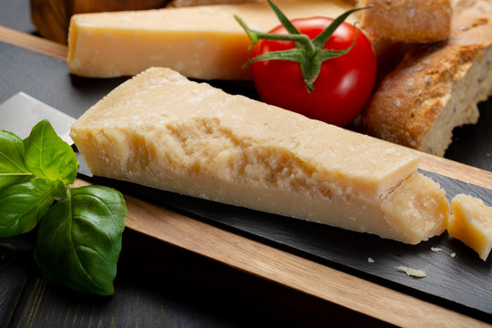 Traditional italian food - aged Italian parmesan hard cheese Parmigiano-Reggiano with cheese knife, tomato, basil, olive oil