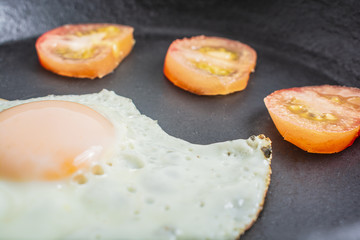 fried egg with tomatoes in a cast-iron frying pan on a wooden table