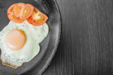 fried egg with tomatoes in a cast-iron frying pan on a wooden table
