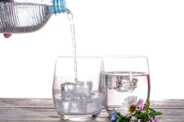 Pouring of sparkling soda mineral drink water in glasses with ice cubes close up copy space