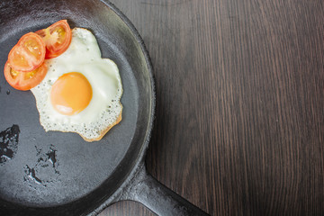 fried egg with tomatoes in a cast-iron frying pan on a wooden table