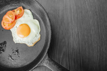 fried egg with tomatoes in a cast-iron frying pan on a wooden table