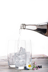 Pouring of still mineral drink water in glasses with ice cubes close up copy space