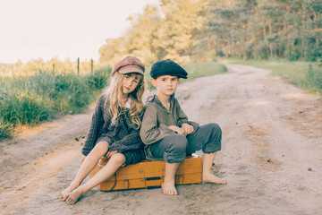 wo children with large yellow suitcase on the road in retro style