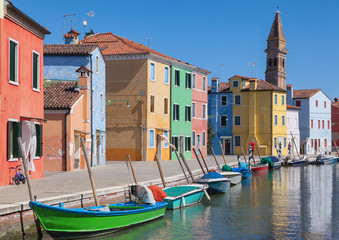 Fototapeta na wymiar Colorfull facade Houses and bell tower on the island of Burano plus reflection in the water. Waterways with traditional boats