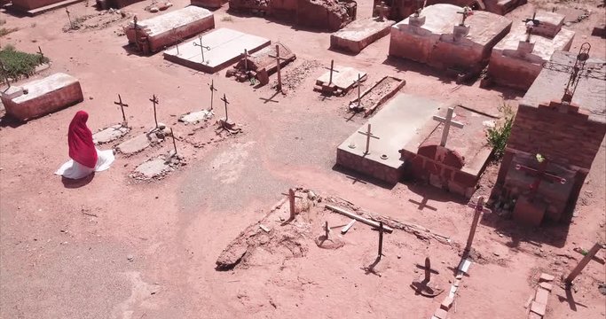 Distraught woman sob on the grave of a family member in cemetery. Aerial view, 4k