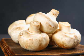 White fresh champignons with parsley on a wooden board on a gray dark table. Mushrooms. Copy the space. Top view.