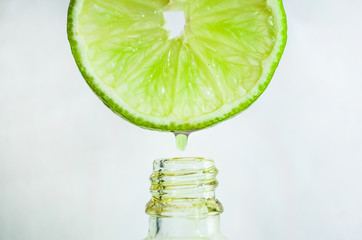 Dripping lime essential oil into bottle on white background