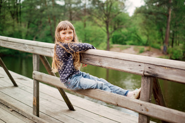 Child girl sitting on a wooden bridge near the water on the river