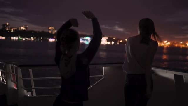 Silhouette of two beautiful young women dancing on ship deck at night. Girlfriends on the boat
