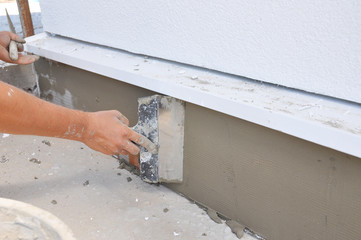 Contractor plastering, repair,  stucco house foundation after styrofoam insulation.