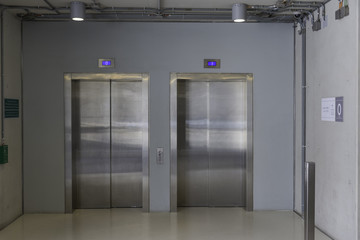 Closed elevators with buttons in corridor with concrete walls.